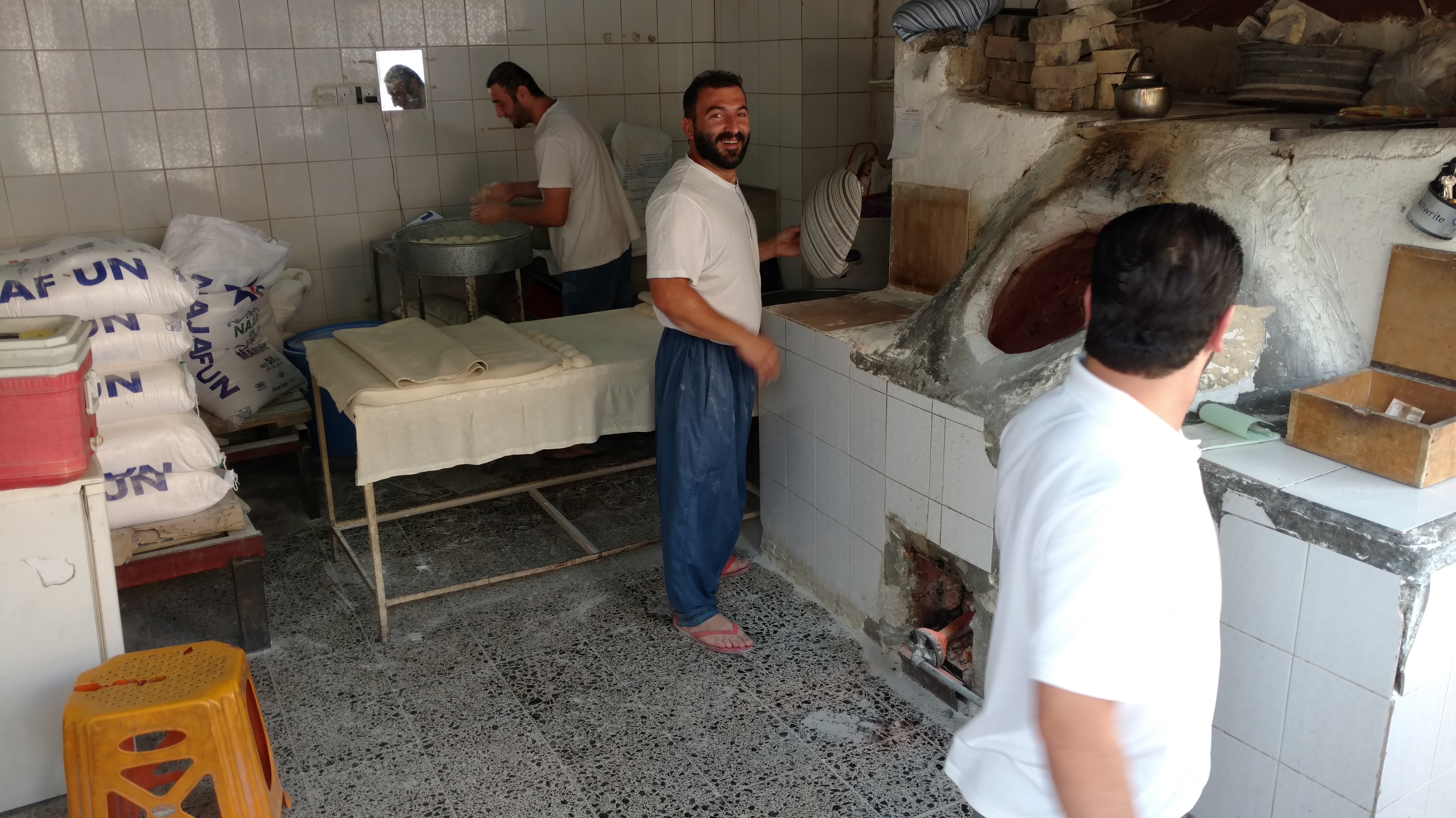 men baking bread in a tandoor-style oven in a bakery in Slemani